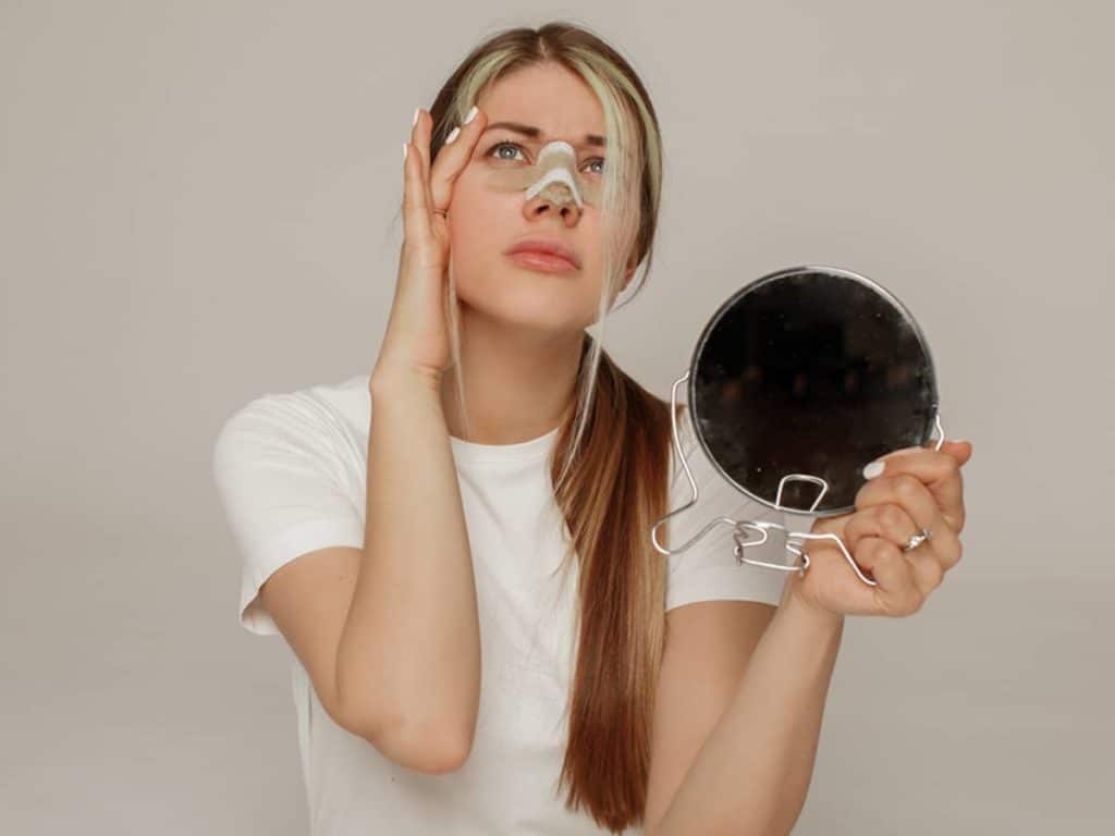 A woman with a nose packing holding a mirror