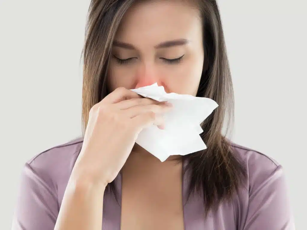 A woman sneezing in relation to how dangerous it is to be sick after rhinoplasty