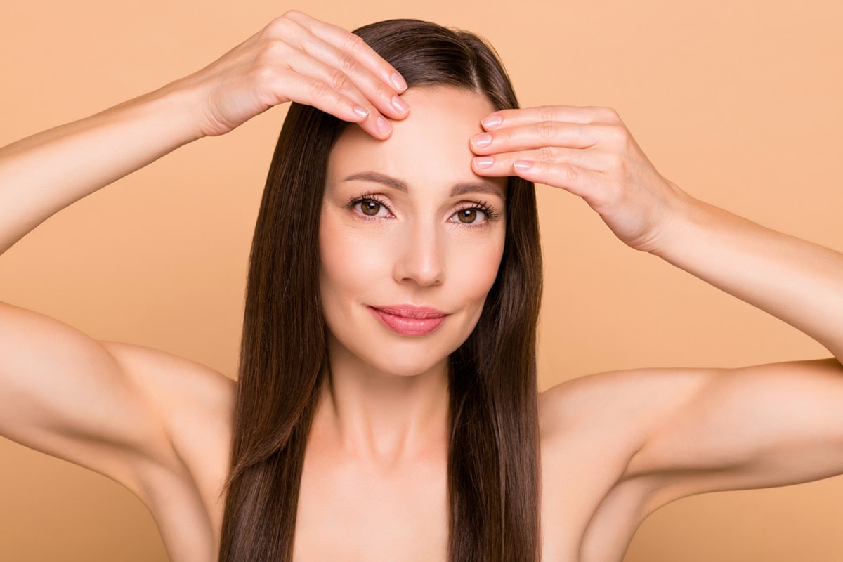 Woman examining forehead after facial surgery, demonstrating recovery.