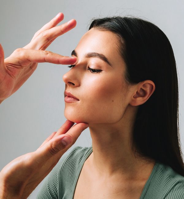 Doctor assessing woman’s nose profile to determine candidacy for rhinoplasty to improve aesthetics and breathing.