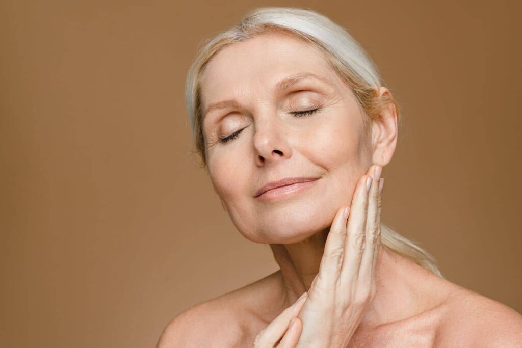 Mature woman touching her face, representing facial aging evaluation and facelift consultation options.
