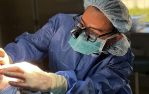 Dr. Jenna Thuman performing surgery in protective gear with magnifying loupes in an operating room.